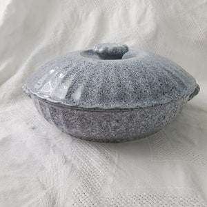 Puede incluir: Una cacerola de cerámica gris con tapa. La cacerola tiene un acabado moteado y un borde acanalado. La tapa tiene un pomo en la parte superior.