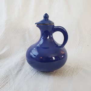 以下が含まれることがあります： 蓋と取っ手のある青い陶器のピッチャー。ピッチャーは丸みを帯びたボディとわずかに広がった注ぎ口を持っています