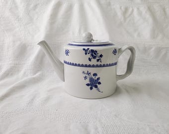 May include: White ceramic teapot with blue floral designs. The teapot features a curved spout, a handle, and a lid with a small knob. The blue floral pattern decorates the body and the lid of the teapot. The teapot is set against a white background.