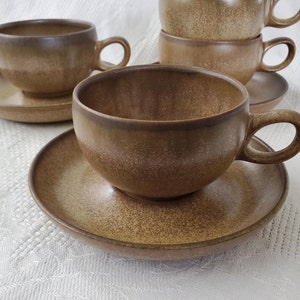 May include: Set of four brown ceramic teacups and saucers. The cups have a rounded shape and a slightly flared rim. The saucers are plain and have a slightly raised edge.