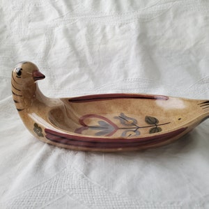 May include: A ceramic serving dish shaped like a bird with a brown and tan glaze. The dish has a floral design painted in red, brown, and blue.