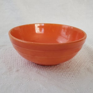 May include: A bright orange ceramic mixing bowl with a rounded shape and a smooth, glossy finish. The bowl has a slight lip around the top edge.