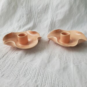 May include: Two peach-coloured ceramic candle holders with a scalloped edge and a round centre hole for a candle.