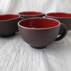 May include: Set of five brown ceramic teacups with red interior glaze.