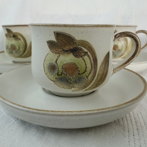 May include: Set of four white ceramic teacups with brown and green floral designs. Each cup has a matching saucer.