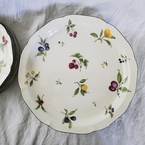 Puede incluir: Un plato de servir de cerámica blanca con un borde negro y un diseño floral con frutas rojas, amarillas y moradas.