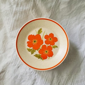 May include: A white ceramic plate with a brown rim features a floral design of orange poppy flowers with green leaves.