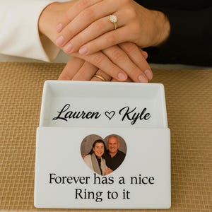 May include: A white rectangular ceramic ring dish featuring the black printed text Lauren heart Kyle inside. The front exterior displays a heart-shaped photograph of a couple and the black printed text Forever a nice Ring to it.
