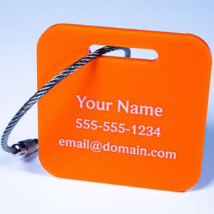 May include: Orange luggage tag with a silver cable loop. The tag has white text that reads "Your Name", "555-555-1234", and "email@domain.com".