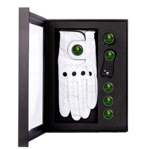 Op de afbeelding: Een witte golfhandschoen met een groen en gouden logo, een zwart golfgereedschap en vier groen en gouden golfbalmarkers in een zwarte geschenkdoos.