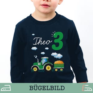 Könnte beinhalten: Marineblaues Langarmshirt mit einem grünen Traktorgrafik, dem Namen "Theo" und der Zahl "3". Der Traktor zieht einen Anhänger mit Heu. Weiße Wolken sind über dem Design verstreut. Das Shirt ist für ein Kind.