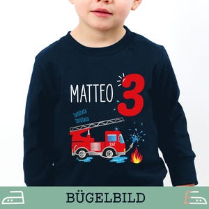 Könnte beinhalten: Marineblaues Langarmshirt mit roter Feuerwehrauto-Grafik, der Zahl 3 und dem Namen "Matteo" in Weiß. Das Feuerwehrauto hat eine Leiter, Wasserspritzer und Flammen. Für Kinder.