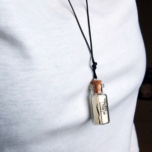 Puede incluir: Un collar con un cord&oacute;n negro y un peque&ntilde;o colgante en forma de botella de vidrio. La botella contiene un trozo de papel con una clave de sol y notas musicales impresas en &eacute;l.