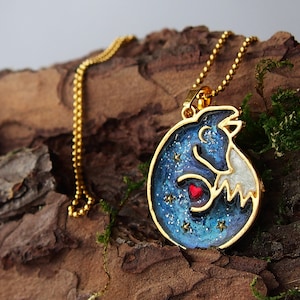 Könnte beinhalten: Eine goldene Kettenkette mit einem blauen und weißen Fuchs-Anhänger. Der Fuchs hält ein rotes Herz und ist von goldenen Glitzersternen umgeben.