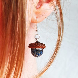 May include: A pair of silver acorn earrings with a blue and white floral design inside the acorn.