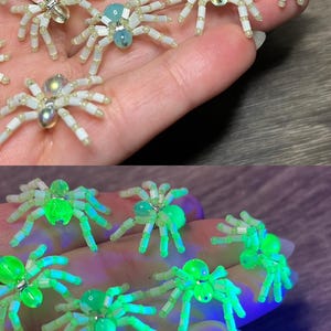 Puede incluir: Decoraciones de arañas hechas a mano con cuentas. Las arañas tienen cuerpos blancos con detalles transparentes, azules y plateados. La imagen inferior muestra las arañas brillando en verde bajo una luz negra. Estas arañas decorativas son perfectas para Halloween.