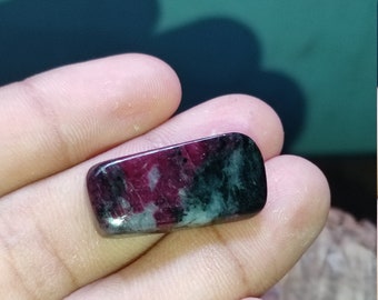 May include: A polished rectangular gemstone featuring a smooth surface with a marbled pattern of deep magenta, dark green, and black tones. The stone has rounded edges and a glossy finish, displaying a distinct color contrast across its surface.