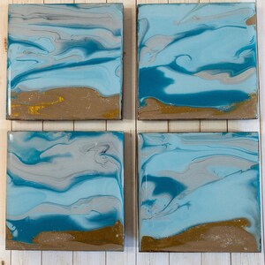 Puede incluir: Conjunto de cuatro posavasos cuadrados con diseños abstractos de pintura azul, gris y dorado. Los posavasos tienen un acabado brillante y son perfectos para agregar un toque de arte moderno a la decoración de tu hogar.