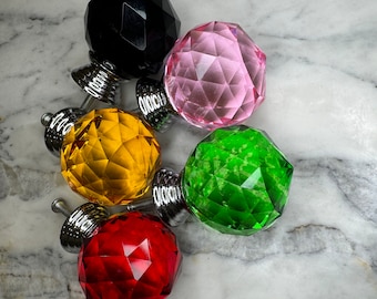 Puede incluir: Cinco pomos de cristal para armario en varios colores, incluyendo negro, rosa, amarillo, verde y rojo. Cada pomo tiene un diseño facetado y una base de metal plateado.