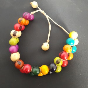 May include: A colorful beaded bracelet with a variety of colors, including red, orange, yellow, green, blue, and purple. The bracelet is made of small, round beads that are strung together on a thin cord. The cord is tied with a knot at the end, allowing the bracelet to be adjusted to fit different wrist sizes.