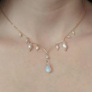 May include: A delicate gold necklace with a teardrop-shaped moonstone pendant and small pearl accents.