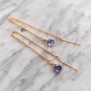Puede incluir: Un par de pendientes de cadena de oro con una pequeña piedra preciosa púrpura que cuelga de cada cadena.