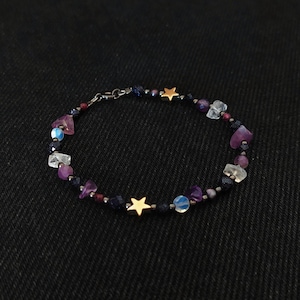 Könnte beinhalten: Ein zartes Armband mit einem Mix aus violetten, blauen und klaren Steinen, akzentuiert mit goldenen Stern-Anhängern.