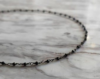 May include: A delicate black choker necklace with small black beads and silver wire.