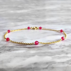May include: A delicate gold chain bracelet with five small, bright pink gemstone beads.