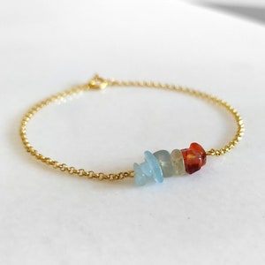 Può includere: Un braccialetto a catena dorata con un gruppo di piccole pietre colorate. Le pietre sono in tonalità di blu e arancio.