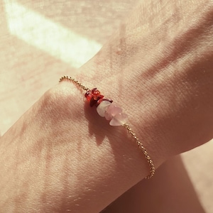 Könnte beinhalten: Ein goldenes Kettenarmband mit kleinen roten und rosafarbenen Edelsteinperlen.