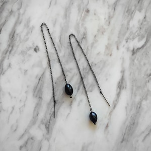 Op de afbeelding: Een paar zwarte oorhangers met zwarte parel accenten.