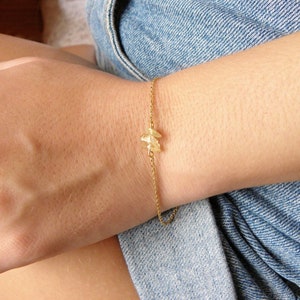 May include: A gold chain bracelet with a small, geometric pendant. The bracelet is worn on a person's wrist.