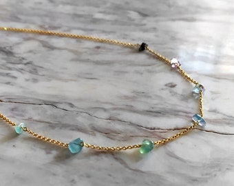 May include: A gold chain necklace with small, colorful gemstones. The necklace features a variety of blue, green, and purple stones.
