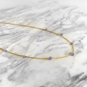 May include: A delicate gold chain necklace with small, light purple gemstone accents.