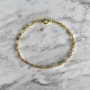 May include: A gold chain bracelet with a delicate, box chain design. The bracelet is made of a thin, gold chain and has a simple clasp.