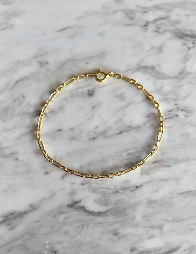 May include: A gold chain bracelet with a delicate, box chain design. The bracelet is made of a thin, gold chain and has a simple clasp.