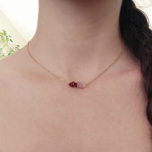 May include: A gold chain necklace with a small cluster of red and pink stones.