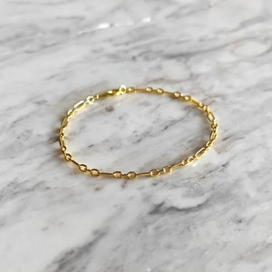 May include: A gold chain bracelet with a delicate, simple design. The bracelet is made of small, linked oval shapes.