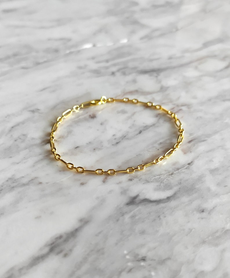 May include: A gold chain bracelet with a delicate, simple design. The bracelet is made of small, linked oval shapes.