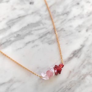 May include: A gold chain necklace with a cluster of pink and red gemstone chips.