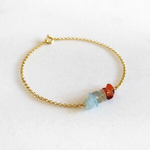 Peut inclure: Un bracelet en cha&icirc;ne dor&eacute;e avec trois petites pierres de forme irr&eacute;guli&egrave;re. Les pierres sont bleues, orange et rouges.