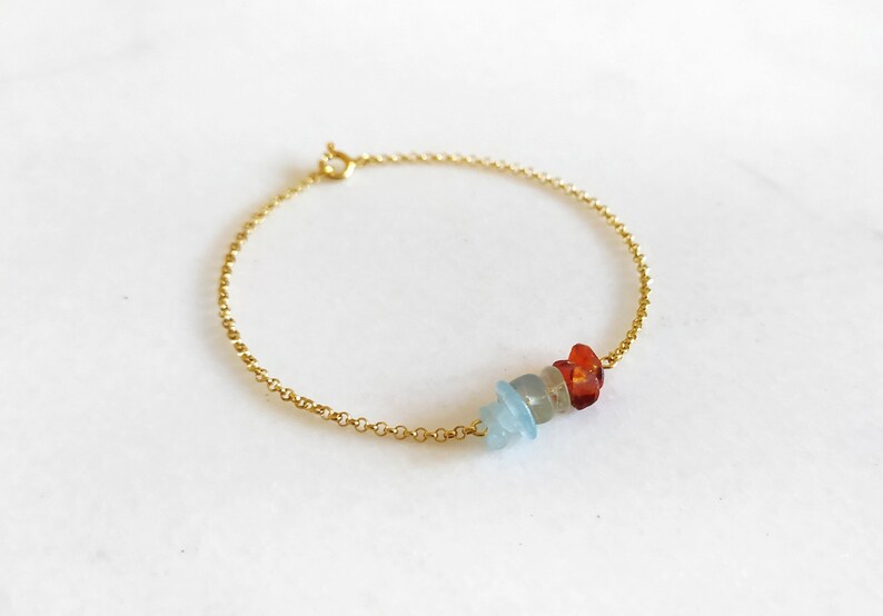 Peut inclure: Un bracelet en cha&icirc;ne dor&eacute;e avec trois petites pierres de forme irr&eacute;guli&egrave;re. Les pierres sont bleues, orange et rouges.