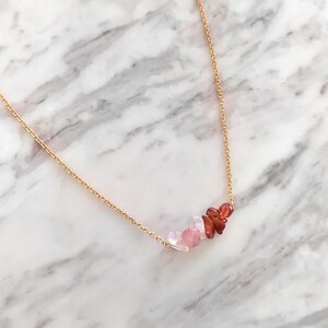 May include: A gold chain necklace with a delicate row of pink and red gemstone chips.