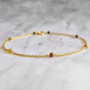 Op de afbeelding: Een gouden kettingarmband met kleine gele en bruine kralen.
