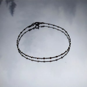 May include: A delicate silver chain bracelet with small square links. The bracelet is made of two strands of chain, and the links are evenly spaced.