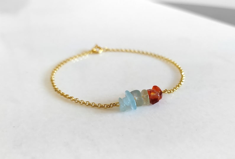 Peut inclure: Un bracelet en cha&icirc;ne dor&eacute;e avec un groupe de petites pierres color&eacute;es. Les pierres sont de nuances de bleu et d'orange.