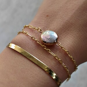 May include: Three gold chain bracelets with a large, round, white pearl charm. The bracelet on the bottom is a snake chain.