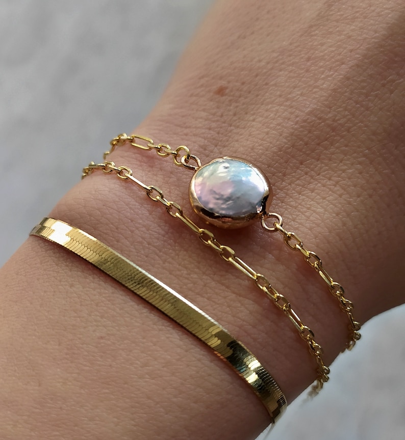 May include: Three gold chain bracelets with a large, round, white pearl charm. The bracelet on the bottom is a snake chain.