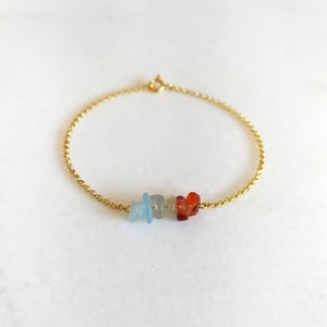Peut inclure: Un bracelet en cha&icirc;ne dor&eacute;e avec une rang&eacute;e de petites pierres color&eacute;es. Les pierres sont bleues, vertes et orange.
